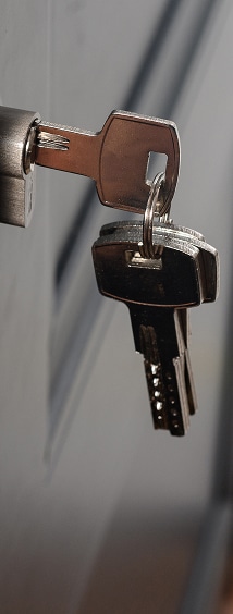 Clé de haute sécurité insérée dans un cylindre de serrure sur une porte moderne avec un trousseau suspendu.