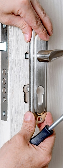 Installation d'une poignée de porte : Guide de montage Mains installant une poignée de porte en métal brossé avec un tournevis sur une porte blanche.