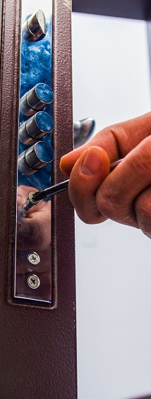 Serrure de sécurité multipoint : installation et réglage Main serrant une vis sur la têtière d'une serrure de sécurité multipoint avec un tournevis.