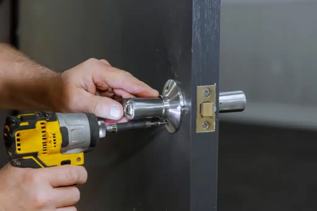 Comment Installer une Poignée de Porte avec une Perceuse Installation d'une poignée de porte en métal avec une perceuse électrique sur une porte en bois gris.