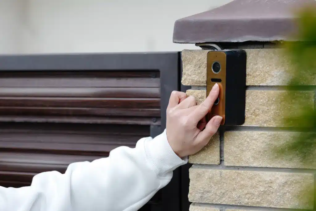 Sonnette vidéo intelligente pour la sécurité de la maison Main appuyant sur une sonnette vidéo moderne installée sur un pilier en briques près d'un portail.